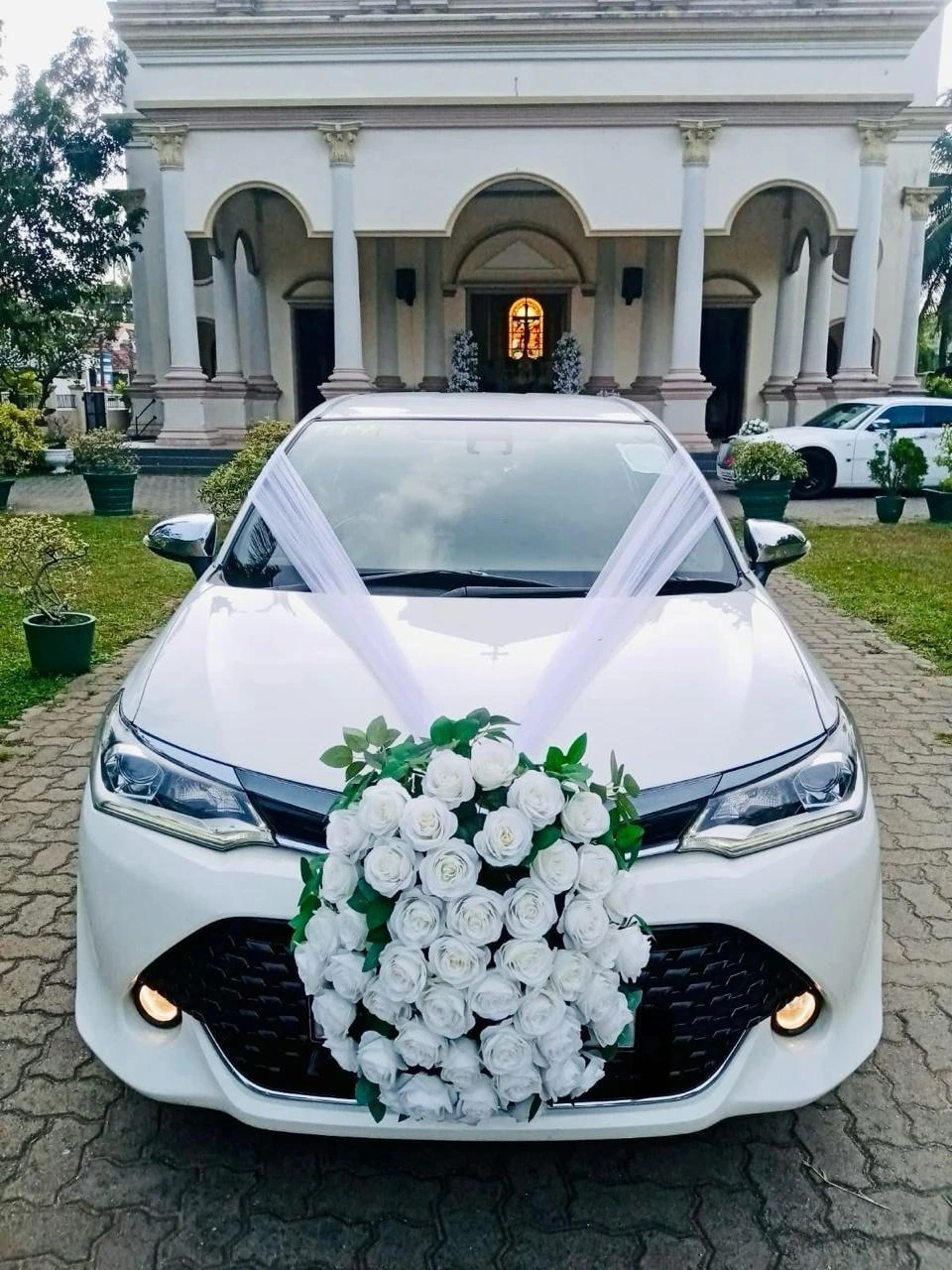 White sedan with a dense white rose bouquet and tulle ribbons in front of a classical building